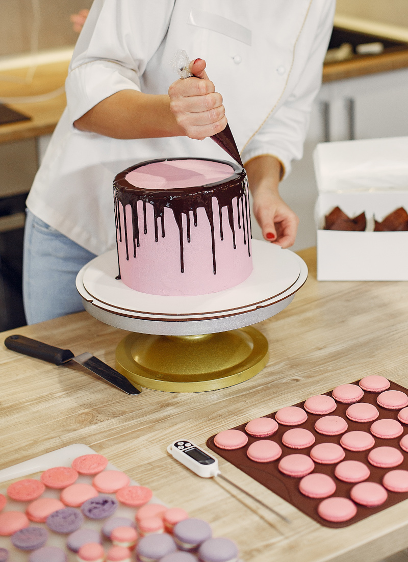 Confectioner in a kitchen. Woman in a uniform. Professional decorates the cake.